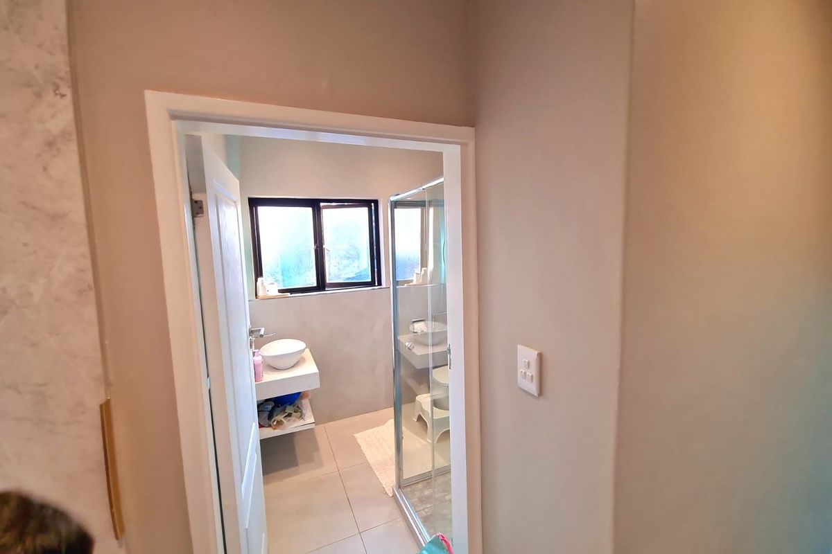 A view into a modern bathroom featuring a wall-mounted vanity with a vessel sink, a glass shower enclosure, and neutral tiled flooring.