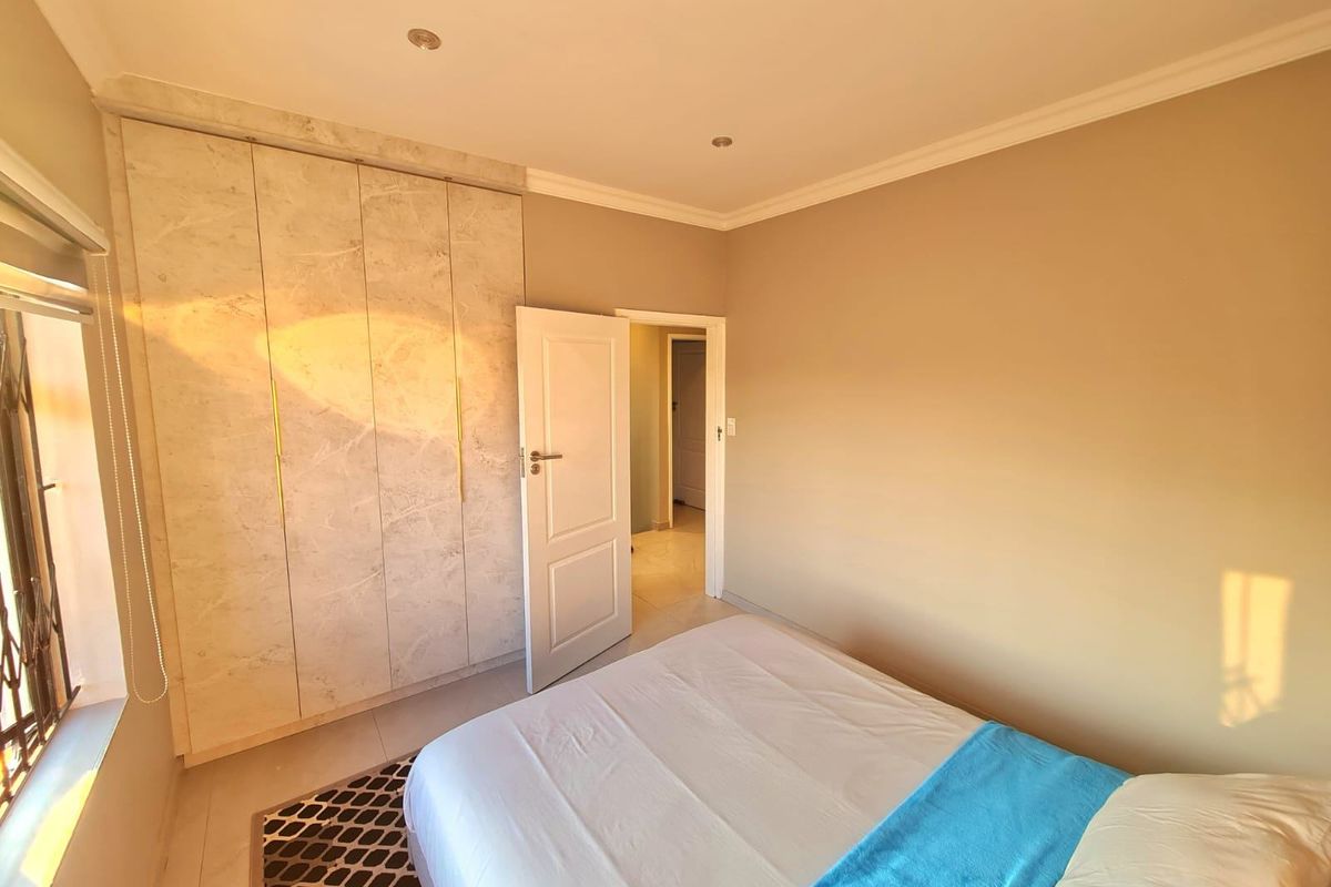 A well-maintained bedroom featuring modern built-in cupboards with a marble-effect finish, recessed downlighting, and neutral tiled flooring.