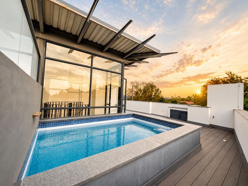 A modern rooftop terrace featuring a sleek plunge pool, composite decking, and expansive glass walls, offering a contemporary outdoor living space with sunset views.