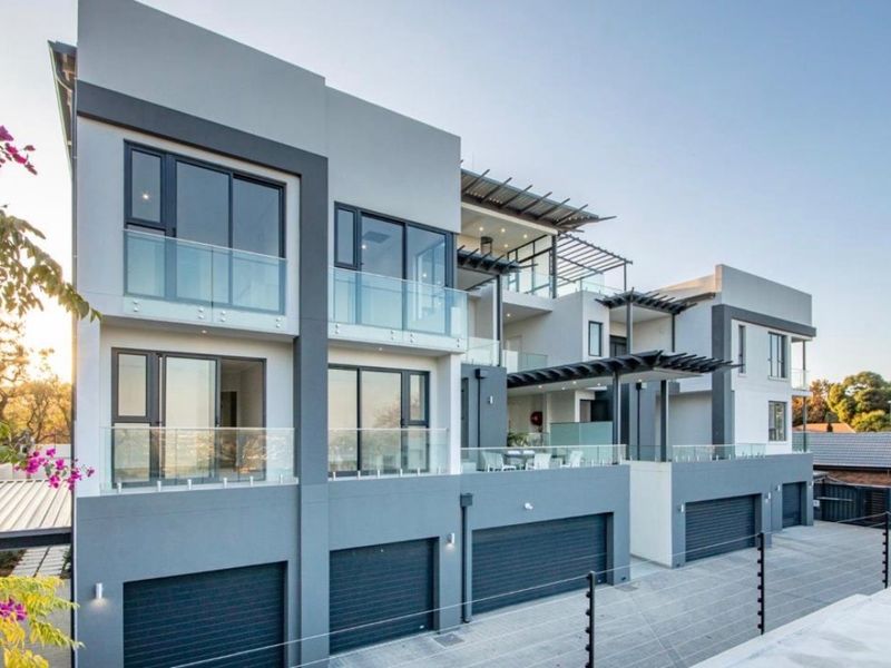 Modern multi-level apartment complex featuring contemporary architectural design, glass balconies, integrated garage access, and clean exterior finishes.