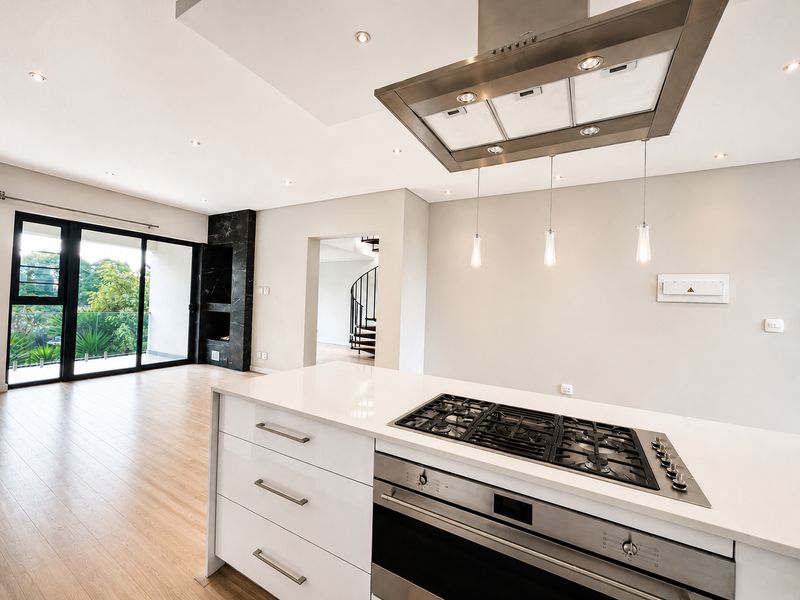 Modern open-plan living area featuring a sleek kitchen island with gas hob, built-in oven, and seamless access to a balcony via sliding glass doors.