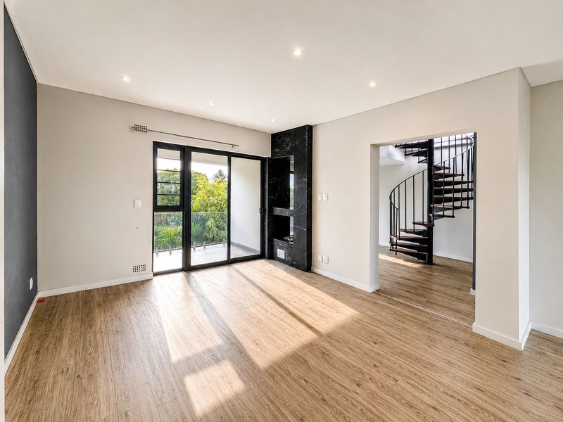 A bright, modern living room featuring laminate flooring, a striking marble-clad fireplace, and a spiral staircase leading to the upper level.