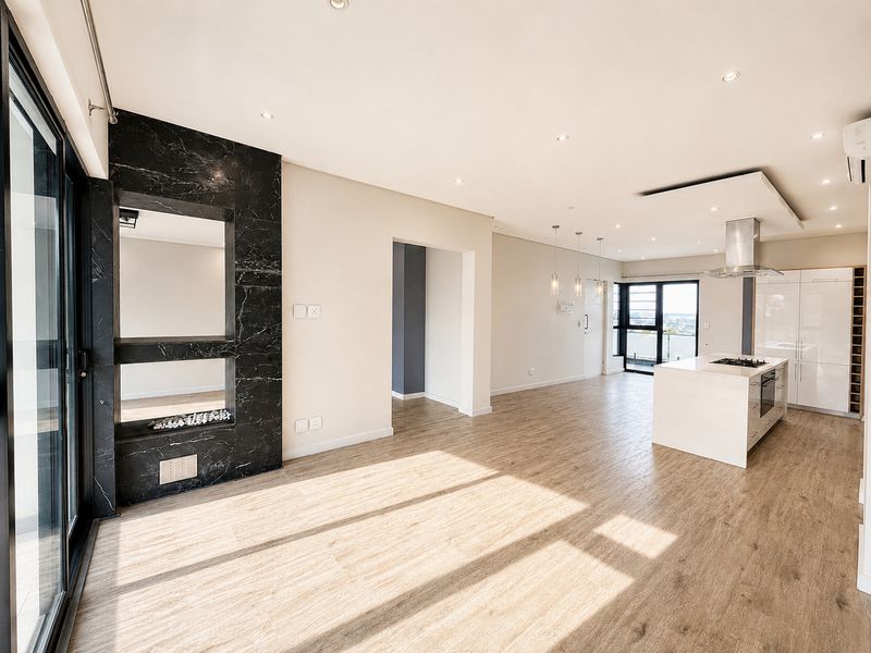 Spacious open-plan living and kitchen area featuring a modern kitchen island, built-in fireplace, recessed lighting, and large sliding doors leading to a balcony.