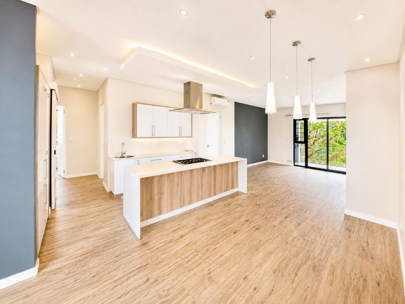 Modern open-plan kitchen and living area featuring a central island with gas hob, sleek cabinetry, recessed lighting, and large sliding doors leading to a balcony.