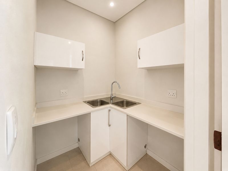 A clean, modern scullery or utility area featuring white built-in cabinetry, a stainless steel corner sink, and ample countertop workspace.