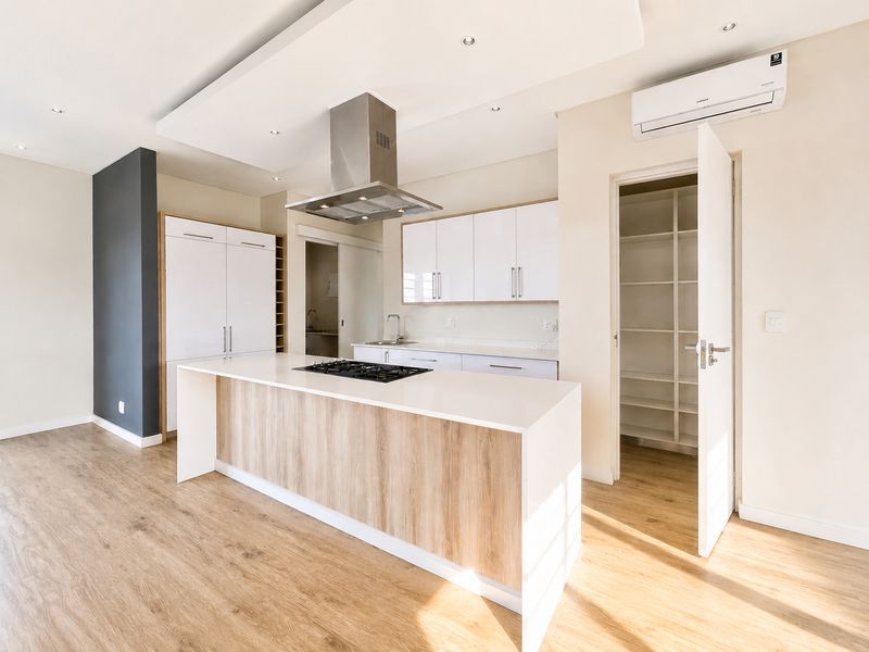 Modern open-plan kitchen featuring a central island with gas hob, sleek white cabinetry, integrated extractor fan, and a convenient walk-in pantry.