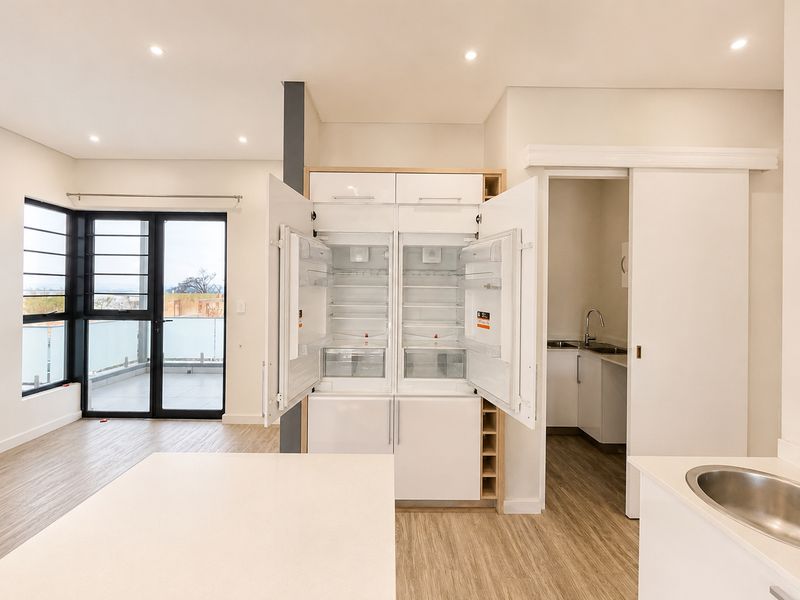 Modern open-plan living area featuring integrated refrigeration, a sleek scullery with sink, and direct access to a private balcony.