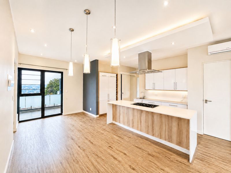 Modern open-plan kitchen and living area featuring a central island, sleek cabinetry, integrated appliances, and direct access to a private balcony.