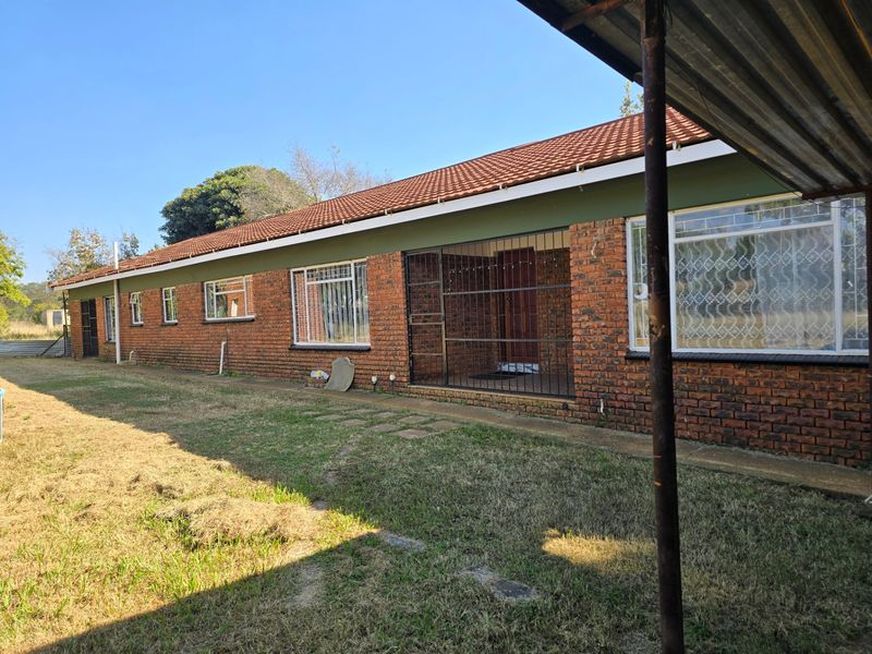 Rear view of a single-story face brick house featuring a tiled roof, security gates, and a concrete walkway along the building perimeter.