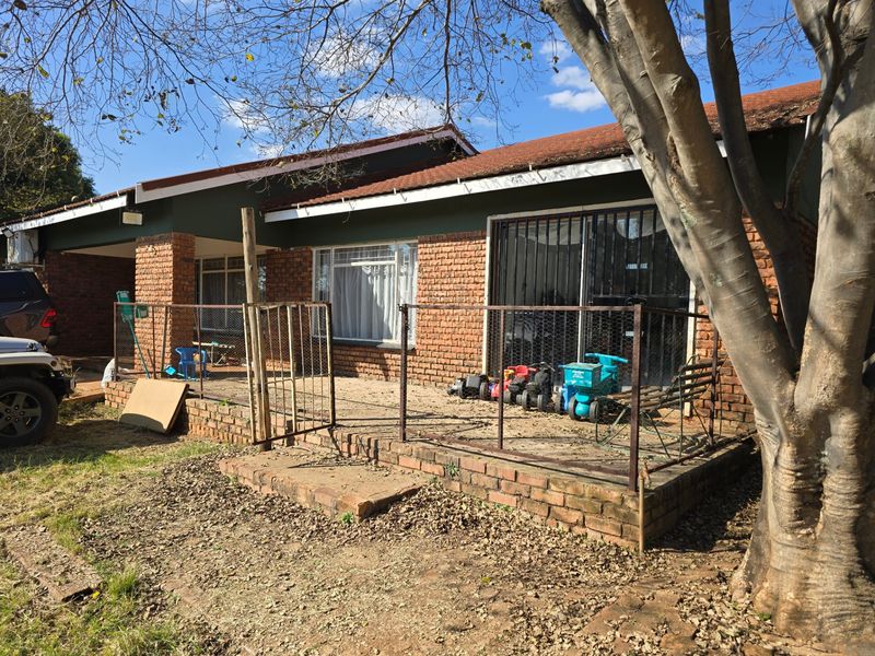 Rear exterior view of a brick house featuring a patio area, security gates, and sliding doors, showing signs of wear and maintenance requirements.