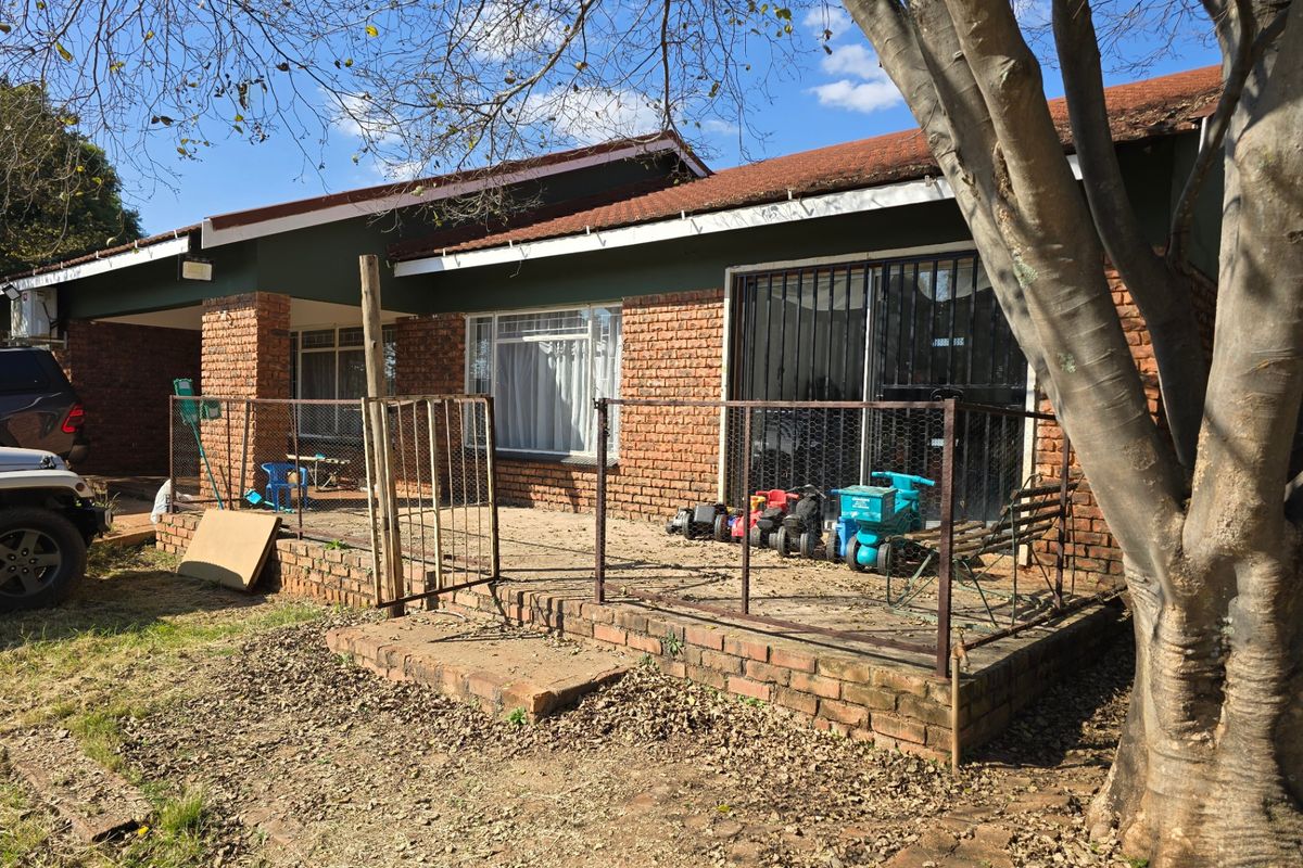 Rear exterior view of a brick house featuring a patio area, security gates, and sliding doors, showing signs of wear and maintenance requirements.