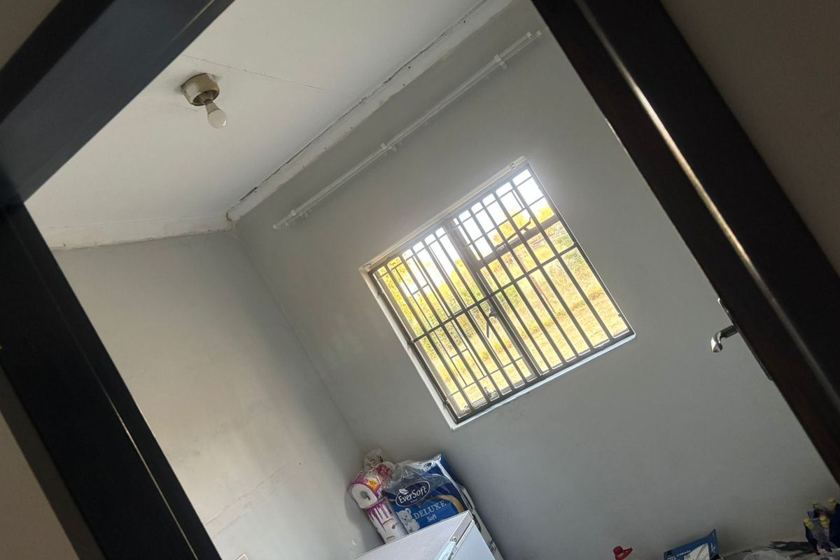 A vacant bedroom featuring a window with security bars and a ceiling-mounted light fixture, requiring cosmetic updates to improve the overall finish.