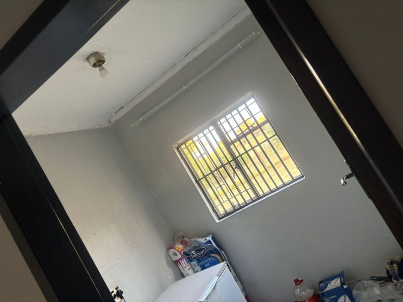 A vacant bedroom featuring a window with security bars and a ceiling-mounted light fixture, requiring cosmetic updates to improve the overall finish.