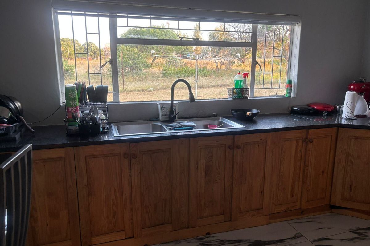 Kitchen area featuring timber cabinetry, dark laminate countertops, a double bowl sink with gooseneck tap, and tiled flooring with a view to the garden.