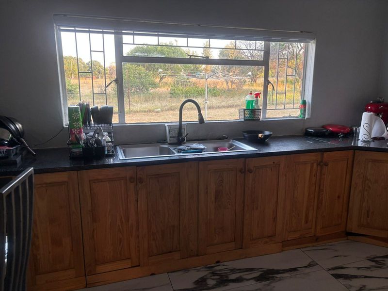 Kitchen area featuring timber cabinetry, dark laminate countertops, a double bowl sink with gooseneck tap, and tiled flooring with a view to the garden.