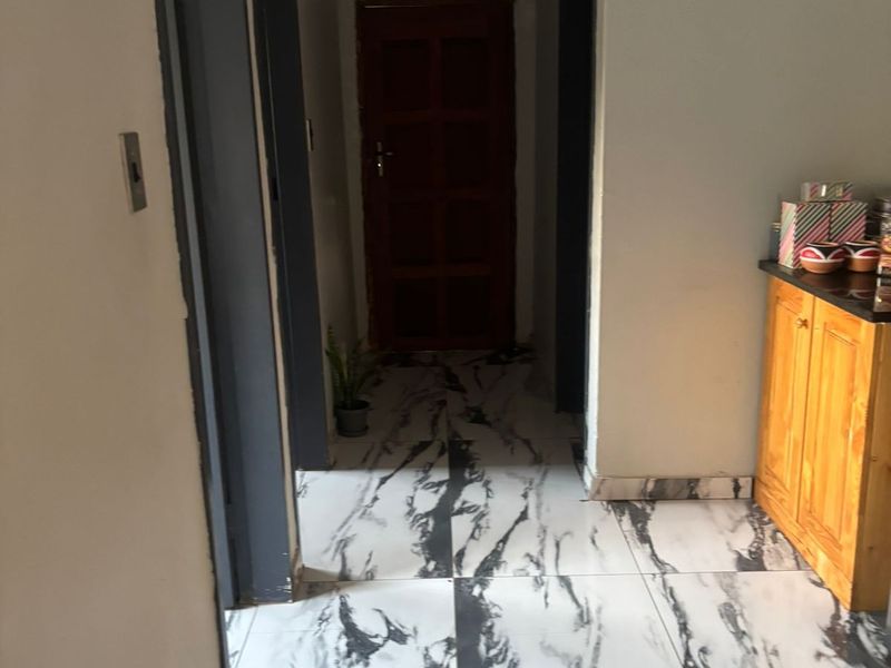 A hallway featuring marble-effect floor tiles, dark-painted door frames, and built-in wooden cabinetry, providing access to multiple rooms.