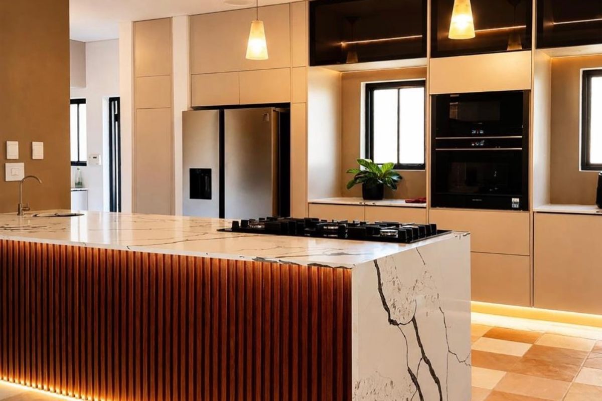 Modern kitchen featuring a large marble-topped island with integrated gas cooktop, sleek cabinetry, built-in appliances, and ambient under-cabinet lighting.