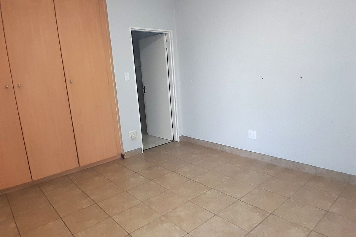 An empty bedroom featuring tiled flooring and built-in wooden cupboards, offering a blank canvas for personalization.