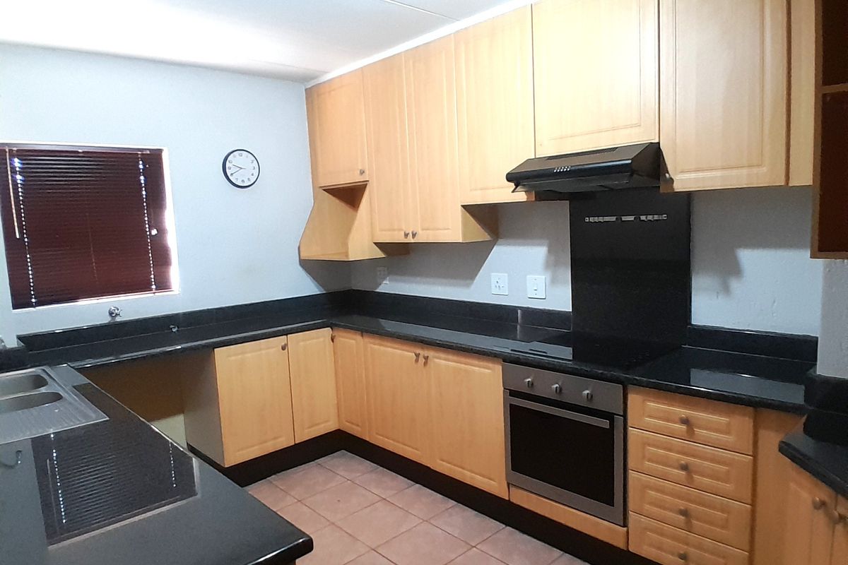 A functional kitchen featuring light wood cabinetry, black granite countertops, built-in oven, extractor fan, and tiled flooring.
