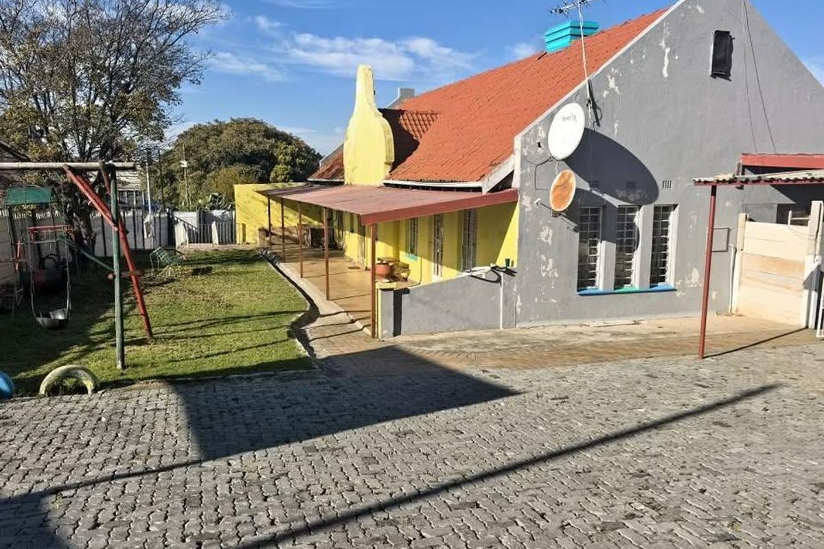 Rear view of the house featuring a covered patio, paved driveway, and a traditional tiled roof structure.