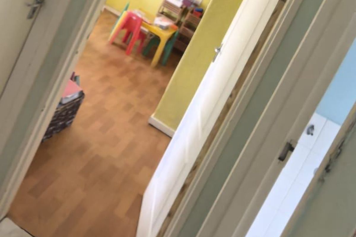 A view through a doorway into a room with yellow walls and laminate flooring, currently utilized as a children's play area.
