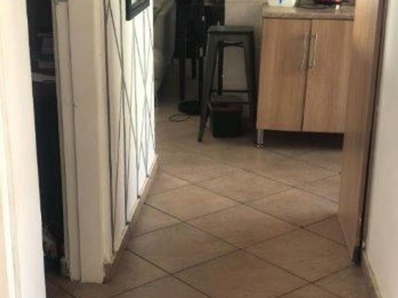 A compact kitchen area featuring tiled flooring, built-in wooden cabinetry, and a tiled backsplash, showing signs of wear and dated finishes.
