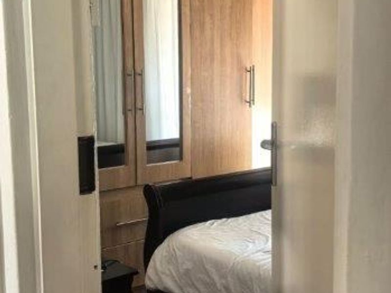 A bedroom featuring built-in wooden cupboards with mirrored panels and tiled flooring, viewed through a doorway.