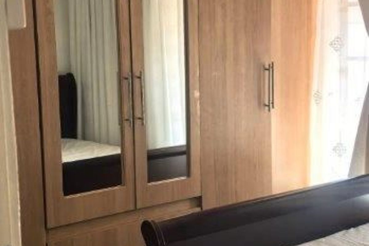A bedroom featuring light wood-finish built-in cupboards with integrated mirror panels and durable tiled flooring.