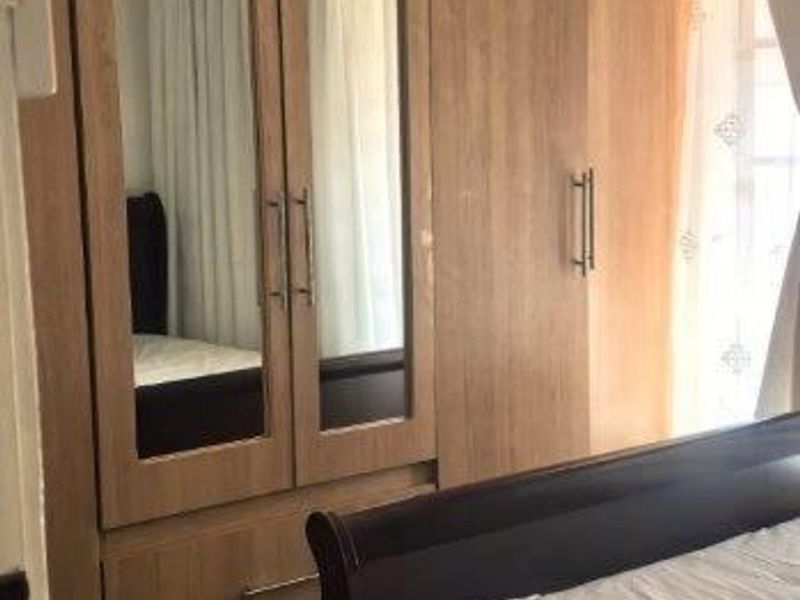 A bedroom featuring light wood-finish built-in cupboards with integrated mirror panels and durable tiled flooring.