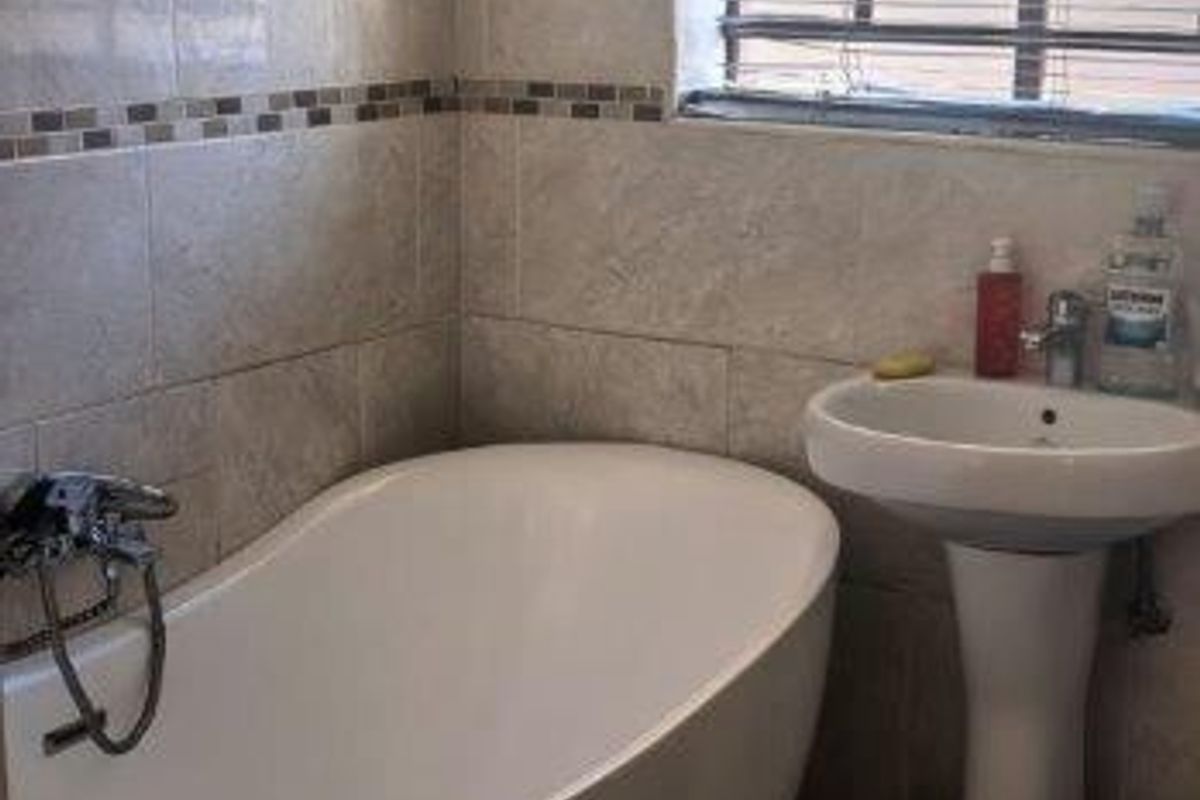 A compact bathroom featuring a modern freestanding bathtub, pedestal basin, and neutral wall tiling with a decorative mosaic border.
