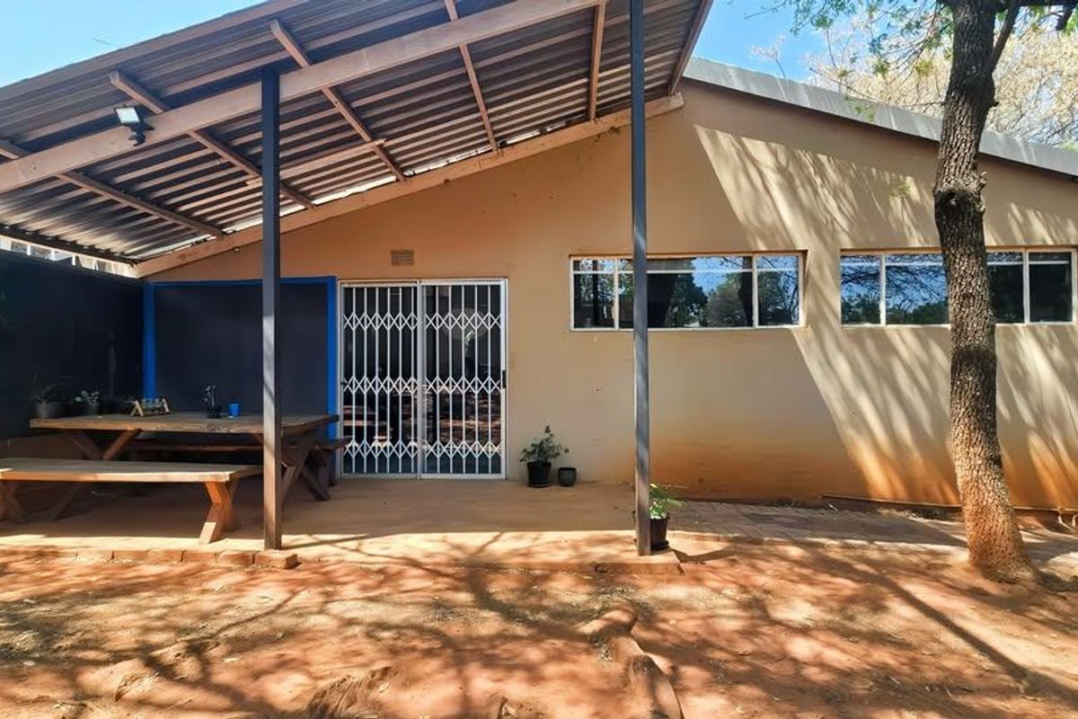 A covered outdoor patio area featuring a corrugated metal roof, security gate access, and paved flooring, providing a functional space for outdoor living.