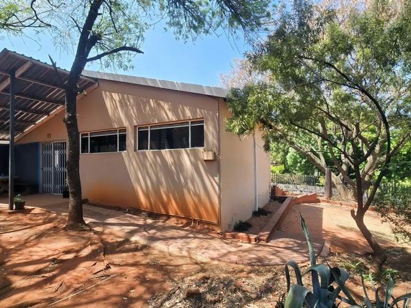 Rear exterior view of the property featuring a covered patio area, security gate, and surrounding garden space with paved pathways.