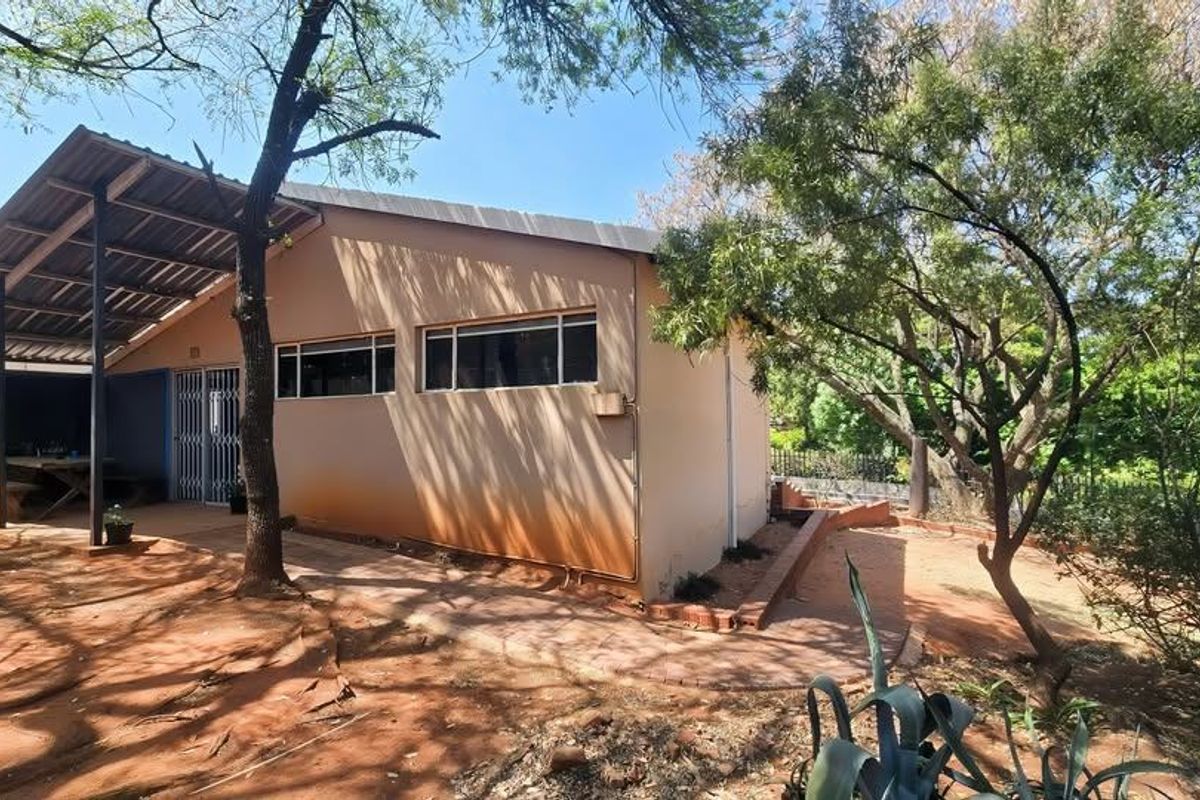 Rear exterior view of the property featuring a covered patio area, security gate, and surrounding garden space with paved pathways.