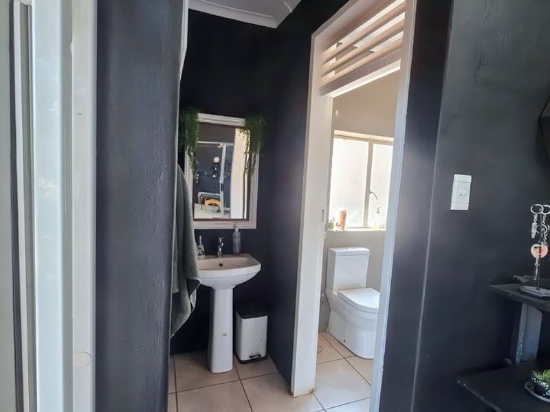 A compact bathroom featuring a pedestal washbasin and a separate toilet area with tiled flooring and dark painted walls.