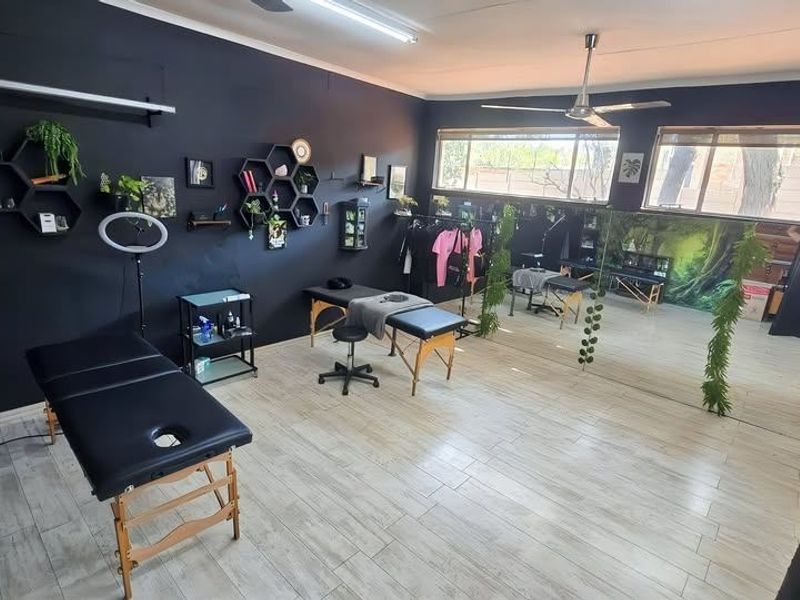 A spacious studio room featuring light-toned tiled flooring, a ceiling fan, and a large wall-mounted mirror, currently utilized as a beauty or treatment space.