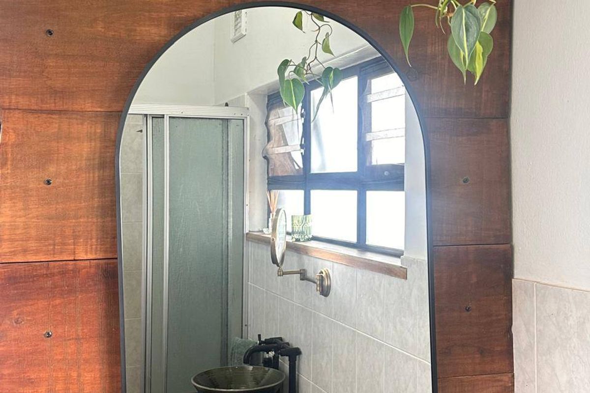 A bathroom featuring a distinctive arched mirror, timber wall paneling, a tiled shower enclosure, and a vessel sink with a modern faucet.