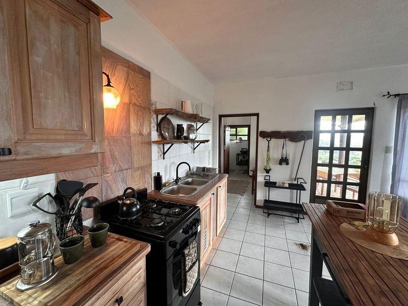 A rustic-style kitchen featuring wooden cabinetry, a gas stove, double basin sink, and tiled flooring with direct access to an outdoor area.
