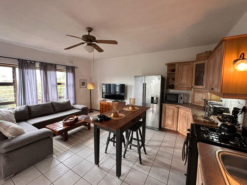 Open-plan living and kitchen area featuring tiled floors, wooden cabinetry, a gas stove, and a ceiling fan, creating a functional and connected living space.