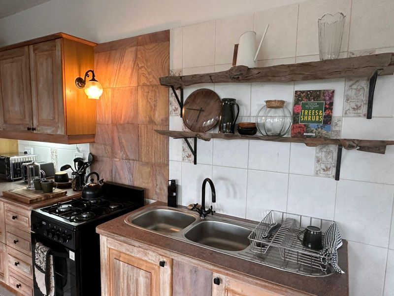 A rustic-style kitchen featuring wooden cabinetry, a double bowl stainless steel sink, gas stove, and natural stone wall accents with floating timber shelving.