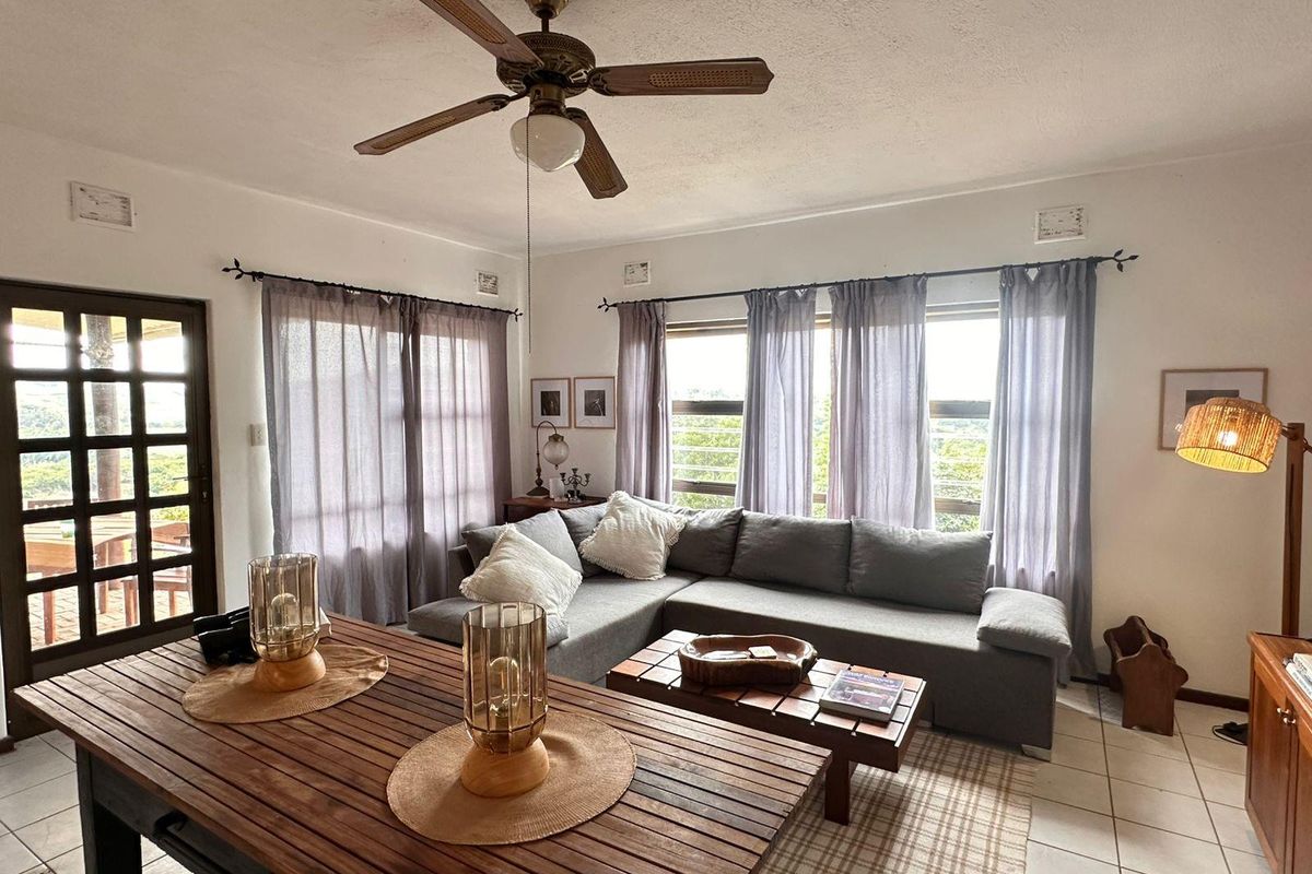 A bright living room featuring tiled flooring, a ceiling fan, and large windows that provide natural light and access to an outdoor area.