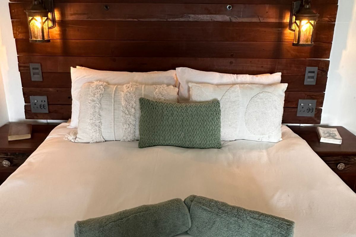 A cozy bedroom featuring a custom timber headboard with integrated lantern-style wall lighting and built-in electrical fixtures.