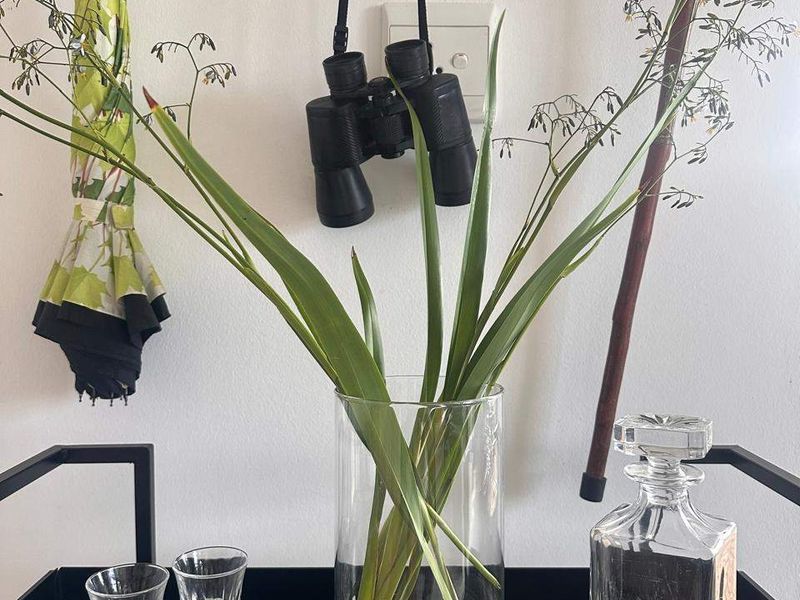 A close-up view of a decorative display featuring a glass vase, glassware, and personal items against a plain wall.