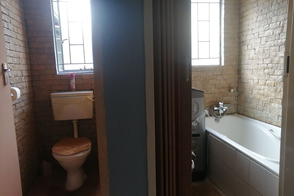 A split-layout bathroom featuring a separate toilet area and a bathtub with stone-clad walls and functional casement windows.