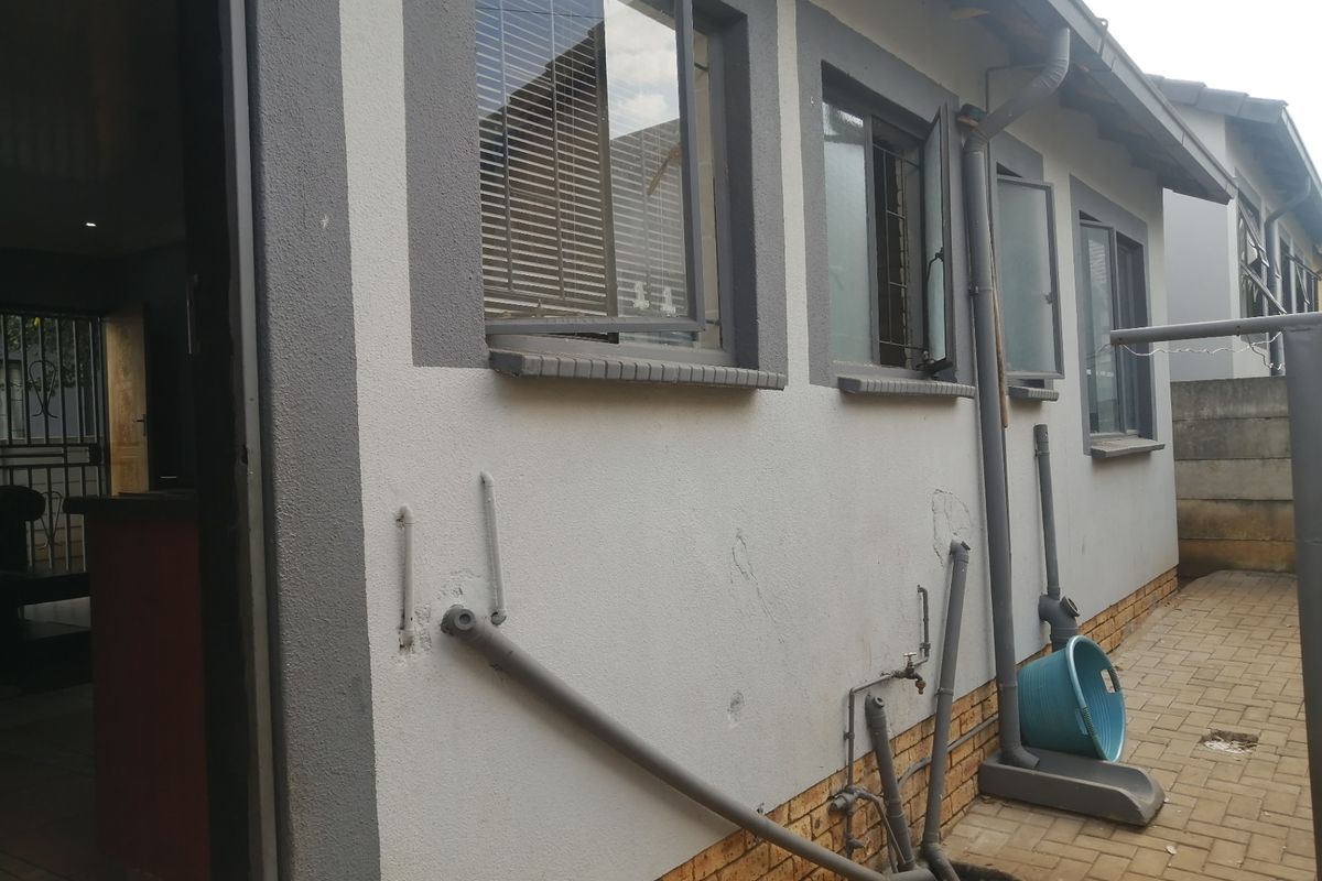 Rear exterior view of the property showing paved walkway, external plumbing fixtures, and casement windows along the side wall.