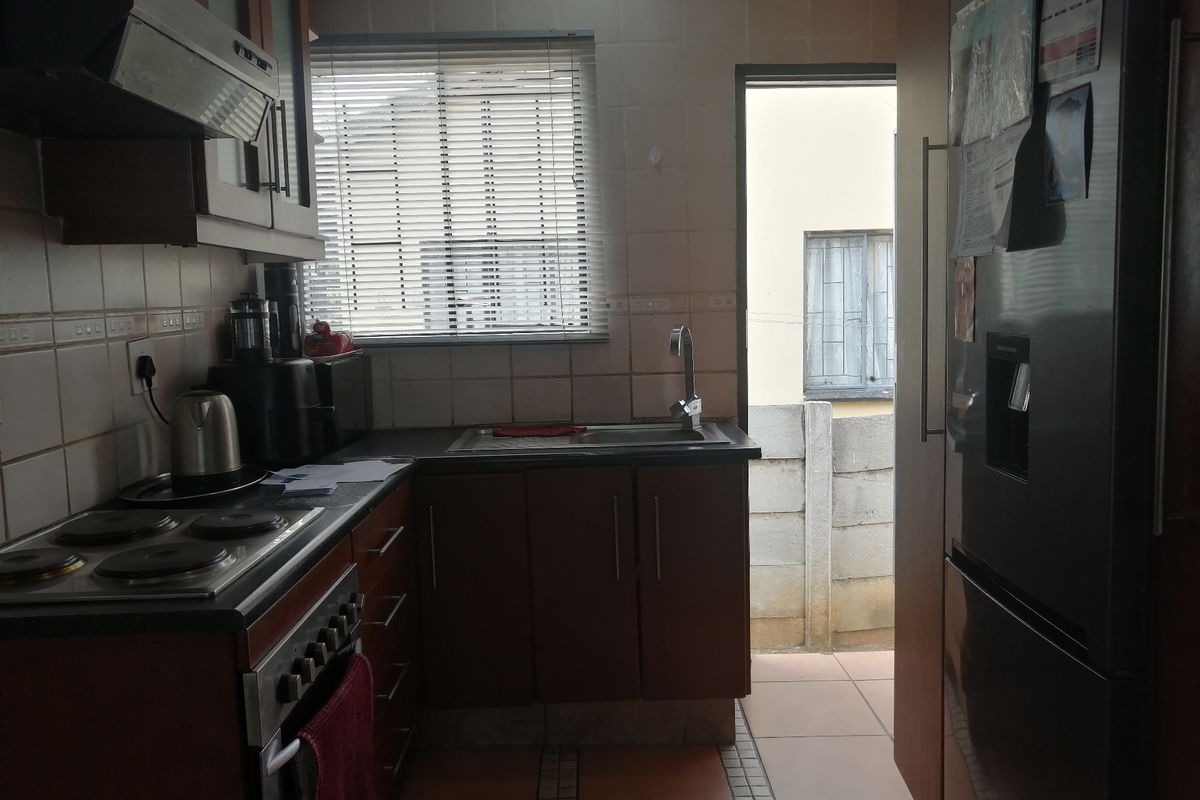 A functional kitchen featuring dark wood cabinetry, a built-in electric hob with extractor fan, tiled backsplash, and direct access to an outdoor area.