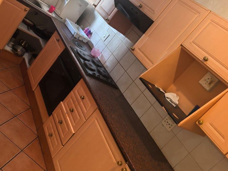 A compact kitchen featuring dated wooden cabinetry, laminate countertops, an electric hob, built-in oven, and tiled finishes throughout.