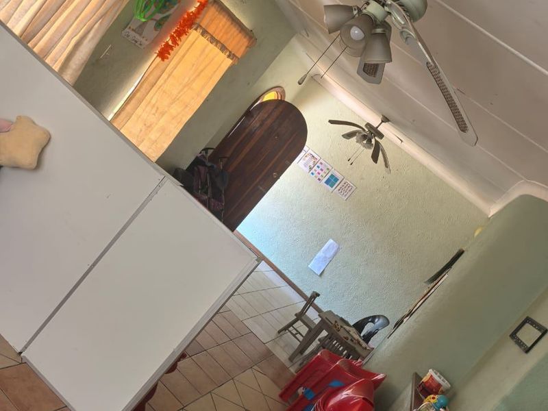 A living area featuring tiled flooring, ceiling fans, and an arched doorway, providing a functional space with potential for modernization.