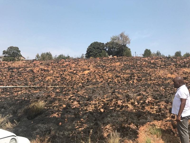 A view of a vacant residential plot featuring sloped, rocky terrain with visible signs of recent fire damage to the ground cover.