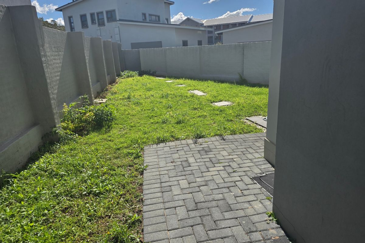 A private rear garden area featuring a paved patio section and a lawn enclosed by high perimeter boundary walls.