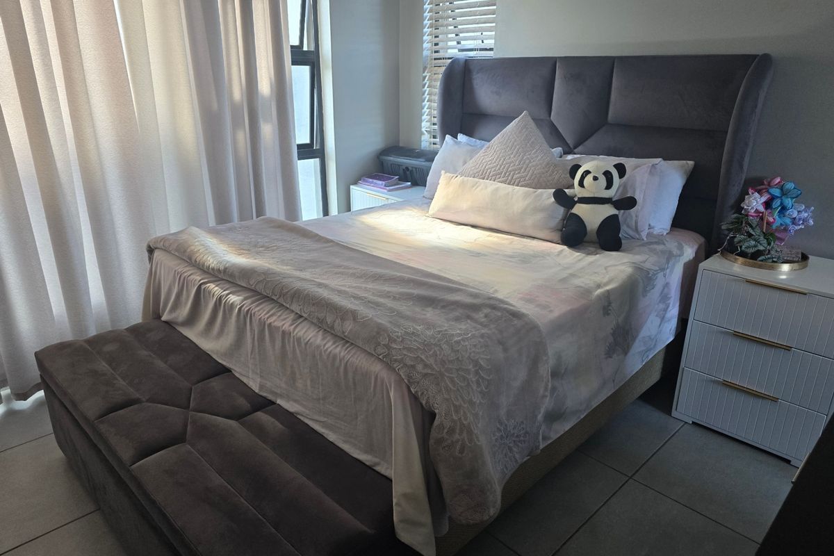 A well-maintained bedroom featuring tiled flooring, neutral walls, and natural light through a large window with venetian blinds.